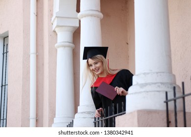 Student In Academic Dress Holds A Diploma In The Library