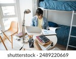 Student asian woman sitting on bed in dorm room college student Work or homework on laptop in university dormitory.