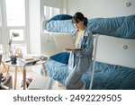 Student asian woman sitting on bed in dorm room college student Work or homework on laptop in university dormitory.