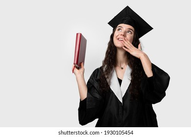 Student With Book In Graduation Robe And Cap Ready To Finish College. Future Leader Of Science. Academician Young Woman In Black Gown Smiling.