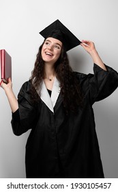 Student With Book In Graduation Robe And Cap Ready To Finish College. Future Leader Of Science. Academician Young Woman In Black Gown Smiling.