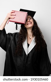 Student With Book In Graduation Robe And Cap Ready To Finish College. Future Leader Of Science. Academician Young Woman In Black Gown Smiling.