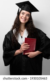 Student With Book In Graduation Robe And Cap Ready To Finish College. Future Leader Of Science. Academician Young Woman In Black Gown Smiling.