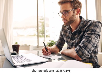 Student Busy Taking Notes Down From His New Laptop Computer While Browsing The Internet With His Morning Coffee