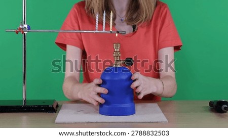 A student demonstrates thermal transfer using a Bunsen burner and a metal rod setup.