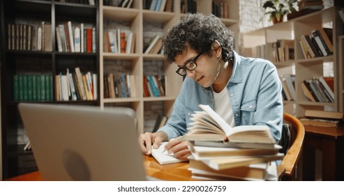 Student is doing research at library using his laptop and books. Nerd is preparing for exams, studying by himself - education, self-study concept close up - Shutterstock ID 2290026759
