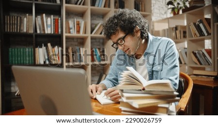 Student is doing research at library using his laptop and books. Nerd is preparing for exams, studying by himself - education, self-study concept close up