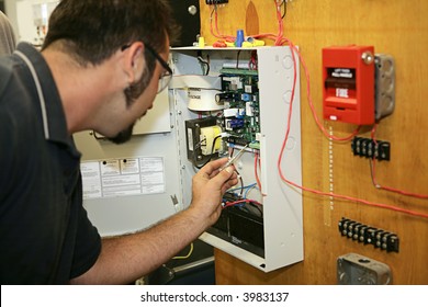 A Student Electrician Wiring A Fire Alarm System At His Technical College.