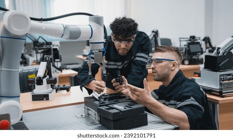 Student engineer Assembling Robotic Arm with computer in Technology Workshop. Service Engineer Holding Robot Controller and Checking Robotic Arm Welding Hardware.