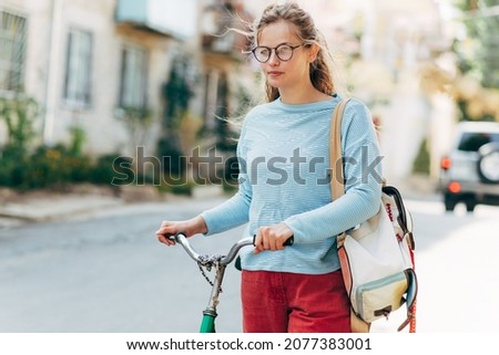 Student female going to the university with a vintage bike on a sunny day outdoors. Pretty woman in casual outfit takes a rest outside after cycling.