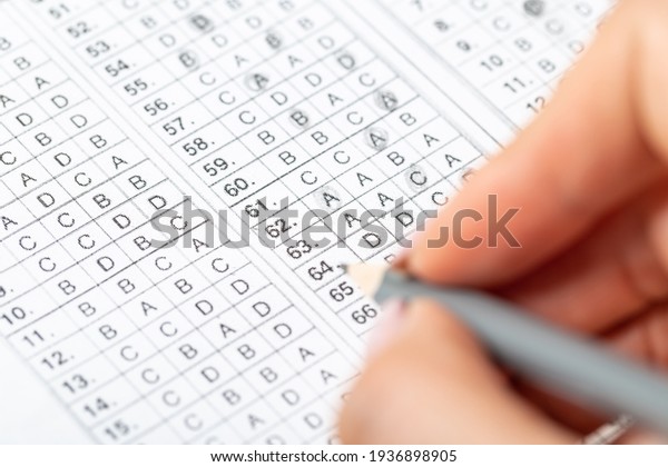 The student fills in\
the answers to the test in the exercise and examination paper with\
a pencil. computer worksheet with pencil in school test room,\
education concept.