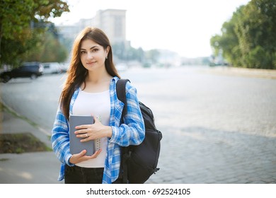 Student girl with books and backpack standing in sunshine on city background. Campus life, holiday, education concept - Shutterstock ID 692524105