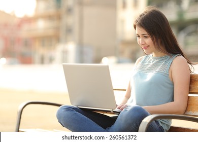 Student Girl Browsing A Laptop And Studying Sitting In A Bench In A Park