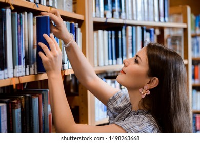 Student girl in dress taking necessary book from the shelf to make research on the matter and prepare for classes of literature - Shutterstock ID 1498263668