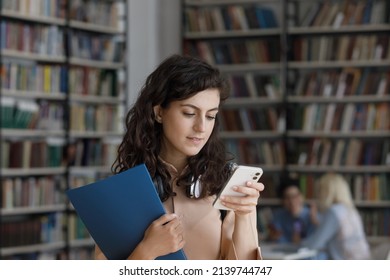 Student Girl Hold Smartphone Standing In Library, Take Break Between Lessons, Check Timetable Online, Use Mobile Application, Chat In Social Media. Generation Z, Modern Tech Usage, Lifestyle Concept