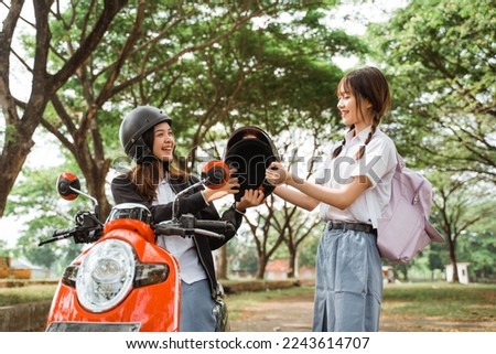Student girl holding a helmet to give to her friend before riding a motorcycle