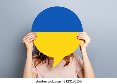 Student Girl Holds Blank White Speech Bubble With Ukrainian Flag Isolated Over Grey Studio Background. Woman Holding A Round Information Piece Of Paper Dialog.