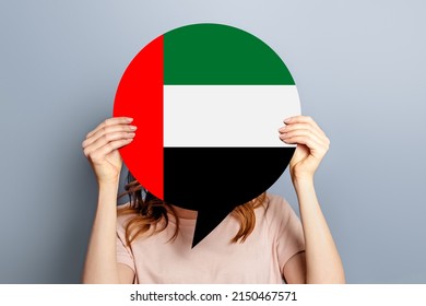 Student Girl Holds Blank White Speech Bubble With UAE Flag Isolated Over Grey Studio Background. Woman Holding A Round Information Poster With Symbol Of United Arab Emirates