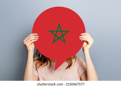 Student Girl Holds Blank White Speech Bubble With The Flag Of Morocco Isolated Over Grey Studio Background. Woman Holding A Round Information Piece Of Paper Dialog