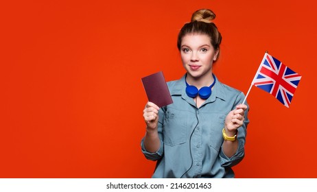 Student girl holds small UK flag and passport in studio on orange background. Study abroad concept. International student exchange program. Learning British English with native speaker.