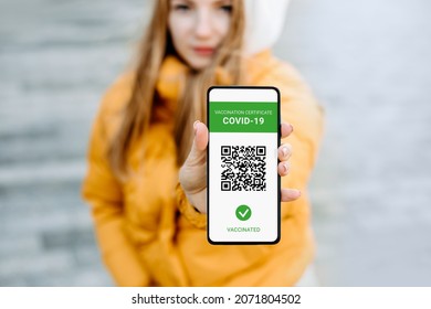 student girl showing a mobile phone screen with an application about vaccination against coronavirus, covid-19, city background - Powered by Shutterstock