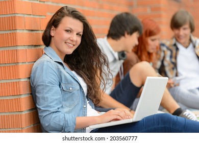 Student Girl Sitting With Laptop Outside Campus Friends In Background