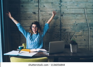 Student girl sitting at table with open notebook and raises hands up while smiling with sincere happiness. Woman overjoyed about successfully completed project on computer. Concept of achievement - Shutterstock ID 1136056844