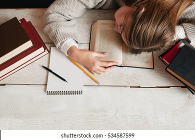 Student girl sleeping on desk with books flat lay. Top view on young tired woman napping on her textbook. Tiredness, exhaustion, education, preparing for exams concept
