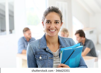 Student girl standing in classroom, holding folders