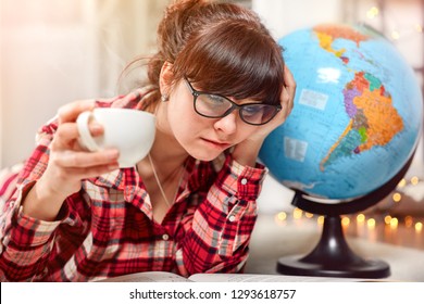 Student girl study homework and reads book. Cup of hot coffee drink in hand. Confused tired face with glasses. Globe world planet Earth. - Powered by Shutterstock