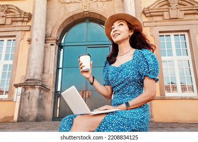 Student Girl Is Working And Studying At A Laptop And Drinking Coffee, Sitting On The Steps At The Entrance To The Campus Or Faculty Of The University. Education In Europe Concept