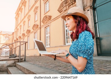 Student Girl Is Working And Studying At A Laptop, Sitting On The Steps At The Entrance To The Campus Or Faculty Of The University. Education In Europe Concept