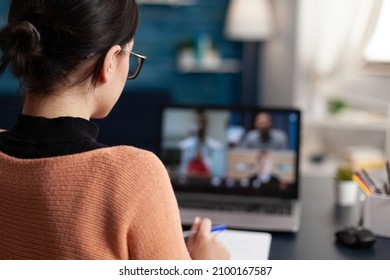 Student in group videocall taking notes. Over the shoulder view of freelancer having briefing video call with team in home office and discussing with colleagues in webcam conference. - Shutterstock ID 2100167587