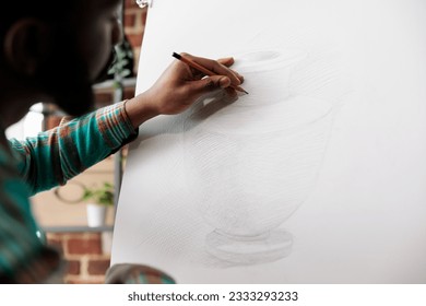 Student guy drawing with pencil on canvas. African American man artist staying focused while creating art in studio or workshop, sitting at easel sketching basic vase using pencil - Powered by Shutterstock