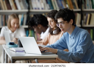 Student guy wear glasses studying in library or classroom, using laptop working on essay, prepare for college exams seated at table with diverse group mates. Education, professionals skills concept
