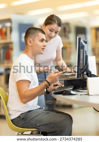 Student guy is working at a computer and preparing for an exam, he turned to a young woman for help. Student helps a classmate with writing a thesis