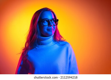 Student. Half-length portrait of young beautiful girl isolated on orange background in neon light, filter. Concept of emotions, facial expression, youth, aspiration, sales. Copy space for ad