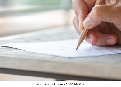 Student Hand Testing Doing Test Exam With Pencil Drawing Selected Choices On Answer Sheet In School Final Exams At College Or University. Taking Multiple Choice For Assessment In Examination Classroom