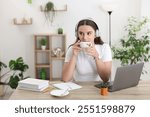 Student in headphones enjoying hot drink while studying at wooden table indoors