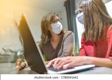 Student And Her Teacher Wearing Protective Mask And Working A Lesson On  A Laptop At Home During Lockdown Due To Covid-19