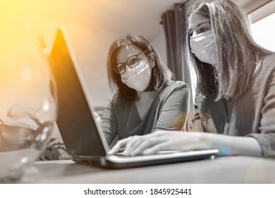 Student And Her Teacher Wearing Protective Mask And Working A Lesson On  A Laptop At Home During Lockdown Due To Covid-19