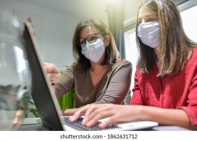 Student And Her Teacher Wearing Protective Mask And Working A Lesson On  A Laptop At Home During Lockdown Due To Covid-19