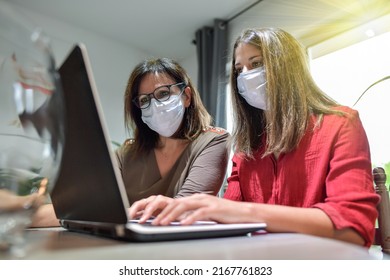 Student And Her Teacher Wearing Protective Mask And Working A Lesson On  A Laptop At Home During Lockdown Due To Covid-19