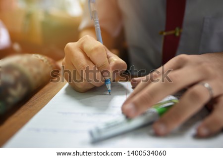 Student holding a pen taking lecture note or doing writing assignment in the classroom; closed up photo of young learner using a pen during the written test in collage or university training center
