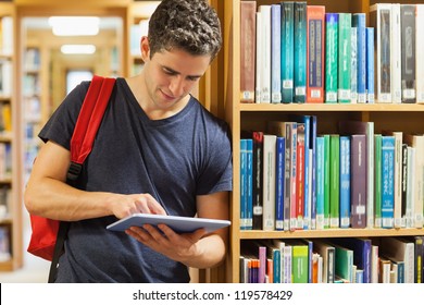 Student leaning against bookshelf holding a tablet pc at the library - Powered by Shutterstock