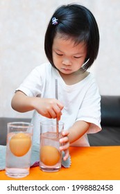 Student learning and doing principles science experiments. Sinking Egg Experiment - Floating eggs with water and salted water. Girl is using metal rod stir to dissolve salt in water. Doing it yourself
