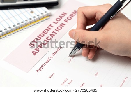A student loan application form rests on a laptop keyboard with a blue ballpoint pen, emphasizing the financial side of higher education and college planning.