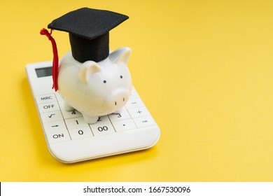 Student Loan Payment Calculation, Scholarship Or Saving For School And Education Concept, White Piggy Bank Wearing Graduation Hat On Calculator On Yellow Background With Copy Space.