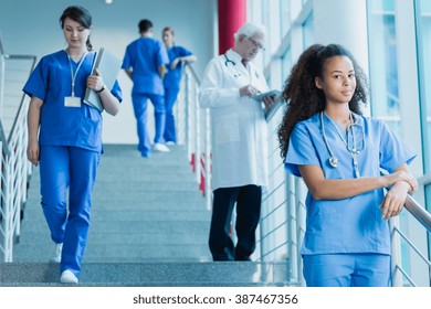 Student of medicine in blue uniform standing on stairs, in the background medic and trainees in uniforms - Powered by Shutterstock