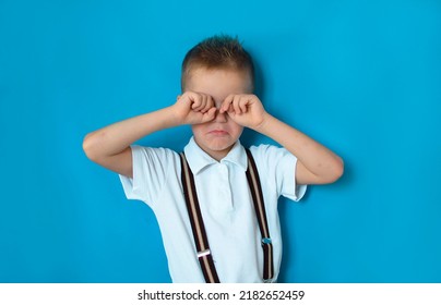 A Student Is Nervous Before The Exam, Isolated On A Blue Background. A Sad, Crying Boy Rubs His Eyes. Baby Crying.